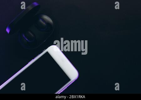 The wireless headphones in the box are unpacked and the cell phone on a black background. Stock Photo