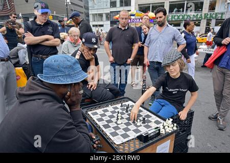 Drawing a crowd, a young man plays chess against an older man. In Union Square Park. Stock Photo