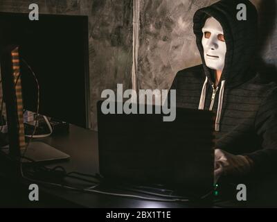 Computer hacker - Man in hoodie shirt with mask stealing data from laptop Stock Photo