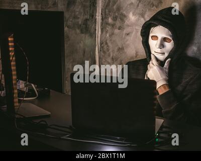 Computer hacker - Man in hoodie shirt with mask stealing data from laptop Stock Photo