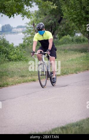 A male cyclist wearing a face scarf mask during the coronavirus plague. Riding on a path in Little Bay Park, Whitestone, Queens, NYC. Stock Photo