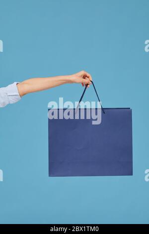 Close-up of female hand holding paper bag isolated on blue background Stock Photo