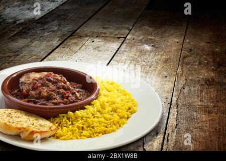 Shot of bowl of chili con carne with rice and garlic bread served in plate over wooden table Stock Photo