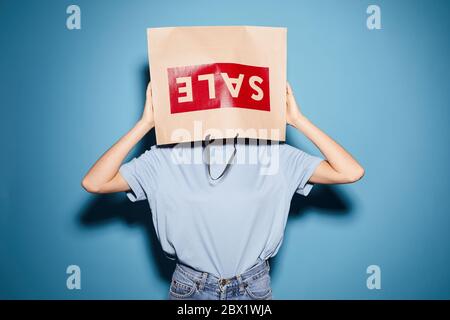 Portrait of young woman wearing paper bag on her head while standing against the blue background Stock Photo