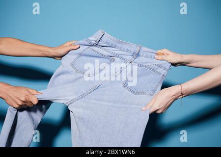 Close-up of two women pulling last jeans on sale in different directions against the blue background Stock Photo