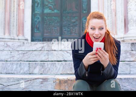 Shocking SMS. Closeup portrait funny shocked young girl looking at phone receiving good news photos message with stunned emotion on face sitting on th Stock Photo