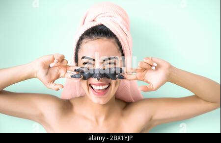 Happy smiling girl applying facial charcoal mask portrait - Young woman having skin care cleanser spa day Stock Photo
