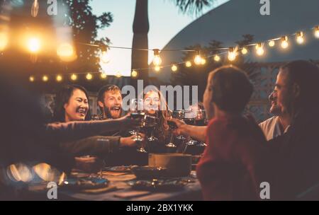 Happy family dining and tasting red wine glasses in barbecue dinner party - People with different ages and ethnicity having fun together Stock Photo