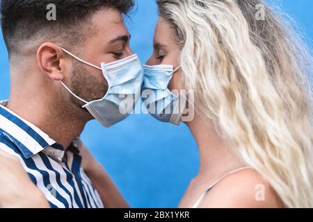 Young couple kissing while wearing face surgical mask during corona virus outbreak - Man and woman with facemask having romantic moments Stock Photo