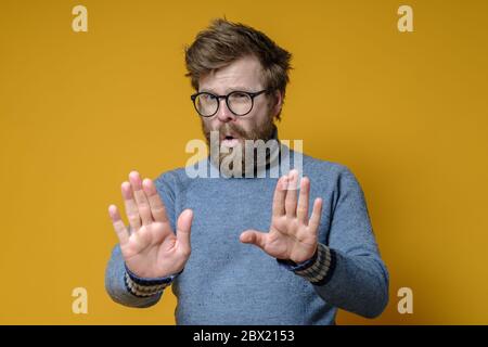 Calm, confident man makes a stop gesture with hands. Shaggy hipster in an old sweater makes a calming signal with palms. Stock Photo