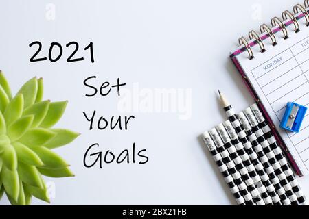 weekly organizer planner, sharp pencil surrounded by dull pencils and words 2021 Set Your Goals and home plant soft focus, on white background. Stock Photo