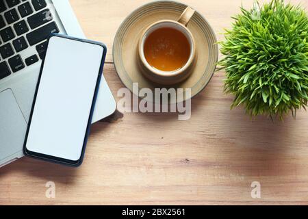 man hand holding smart phone with empty screen .and laptop on table  Stock Photo