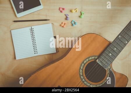Top view of acoustic guitar with blank notebook on wooden table background.vintage effect style picture Stock Photo