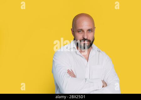 Serious middle-aged man with folded arms and a deadpan expression posing in front of a yellow background Stock Photo