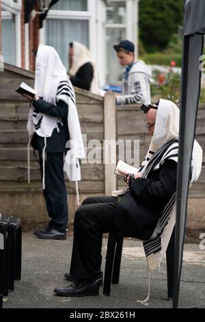 Manchester, UK. 4th June, 2020. Orthodox Jewish men conduct their morning prayers in adjacent gardens in Salford so as to comply with new rules allowing 6 people to congregate in one garden but still achieve a minyan, a quorum of ten Jewish adults required for certain religious obligations, Manchester, UK. Credit: Jon Super/Alamy Live News. Stock Photo