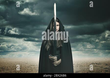 Beautiful dark woman with sword in a desert and stormy landscape. Fantasy and surreal Stock Photo