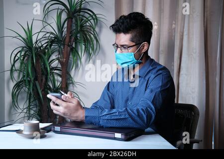 Businessman in face mask working using smart phone at home  Stock Photo