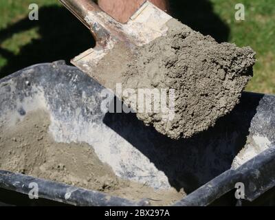 Concrete mortar mixed in black bucket with spade by worker in garden, close up Stock Photo