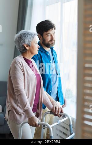 Older son taking care of his senior mother they standing near the window and talking at home Stock Photo