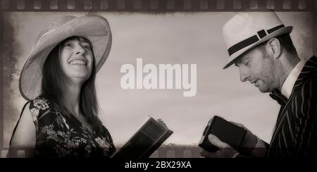 Monochrome, stylised close up UK happy couple in 1940s costume outdoors in summer sunshine. Man is photographing wife using vintage Box Brownie camera. Stock Photo