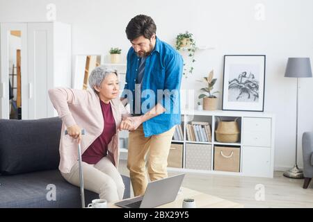 Man helping senior woman to stand up he support her while they are in the living room at home Stock Photo