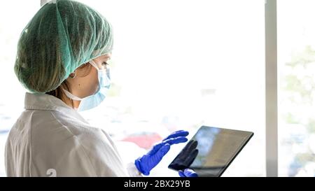 Cropped shot of an unrecognizable female nurse using a digital tablet while standing in a hospital. whit a mask Stock Photo