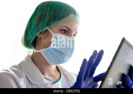 Cropped shot of an unrecognizable female nurse using a digital tablet while standing in a hospital. whit a mask Stock Photo