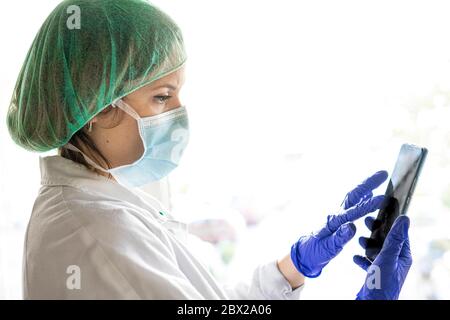 Female nurse using smart phone with mask. Medical professional is wearing uniform. She is looking away at hospital Stock Photo