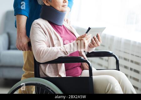 Close-up of senior woman in bandage on her neck sitting in wheelchair and using digital tablet Stock Photo