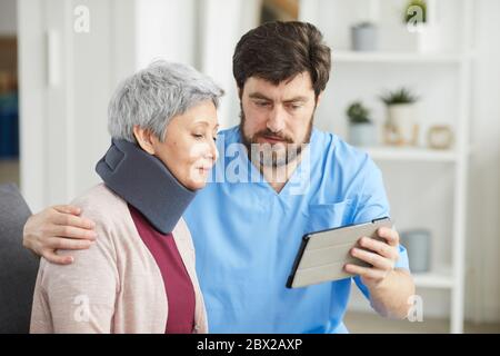 Mature bearded doctor showing something on tablet pc to his senior patient who has a neck injury Stock Photo