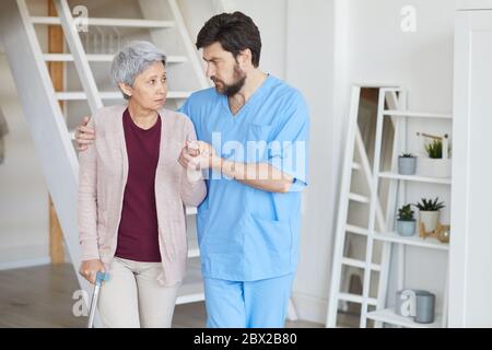 Mature bearded man in uniform caring for senior woman he helping her to move around the room Stock Photo