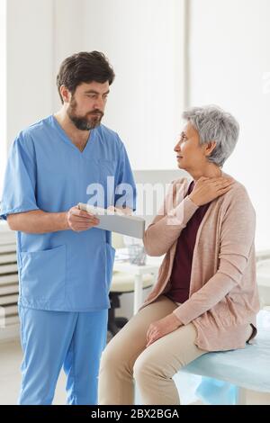 Senior woman has a visit at doctor's office she complaining on the pain in her neck while doctor using tablet pc Stock Photo