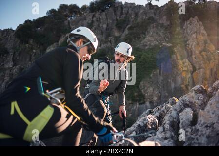 Concept: adventure. Man and woman with helmet, harness. Explaining climbing techniques. Solar luminous flare. Doing via ferrata in the mountains. Stock Photo