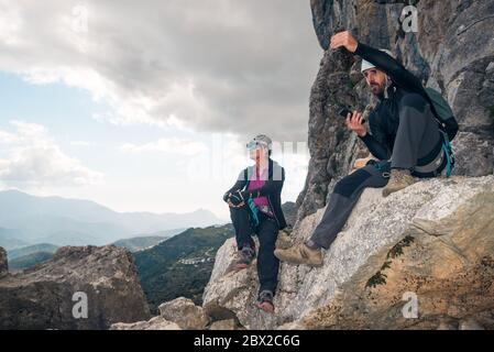 Concept: adventure. Man and woman climbers with helmet and harness. Resting sitting on a rock. Talking and gesturing while looking at the horizon. Doi Stock Photo