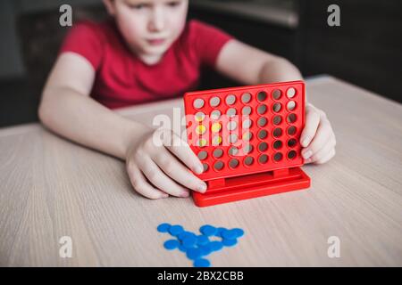 Irish-type red-haired child spends time at the board game 'Four in a line' - the boy focuses on the intellectual game - the development of logic in th Stock Photo