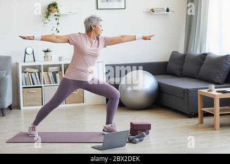 Senior woman standing on exercise mat exercising during sports training in the living room at home Stock Photo