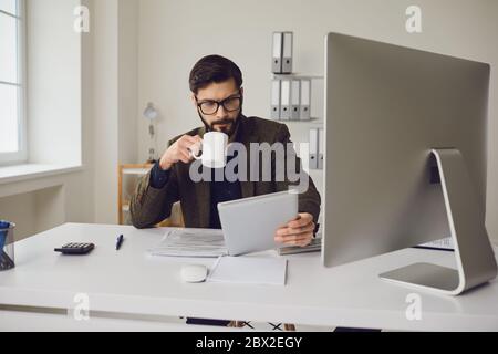 Businessman worker drinking a coffee mug while sitting at a table with a computer working in the office. Stock Photo