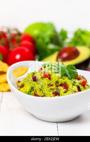 Bowl of Avocado Guacamole Mexican Dip with Avocado, Lime, Tomato, Cilantro with Fresh Ingredients on a Table with Tortilla Chips. Stock Photo