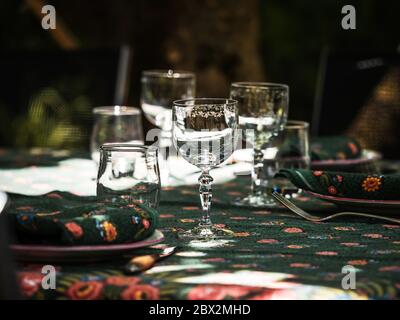 A simple but elegant tablecloth and cutlery laid out on it. Crystal glasses in the sun. Everything is ready for lunch in the garden.France. Stock Photo