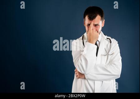Portrait of male doctor with stethoscope in medical uniform wondering posing on a blue isolated background. Stock Photo