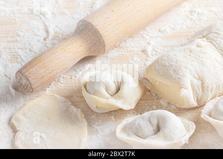 Raw homemade delicious traditional italian ravioli with meat and a rolling pin on wooden surface. Uncooking dumplings with minced meat and dough on ta Stock Photo