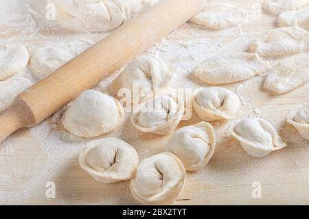 Uncooking dumplings with minced meat and dough on table sprinkled with flour. Raw homemade delicious traditional italian ravioli with meat and a rolli Stock Photo