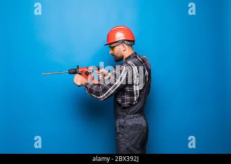 Young male worker or builder with working with electric drill or perforator over blue background Stock Photo