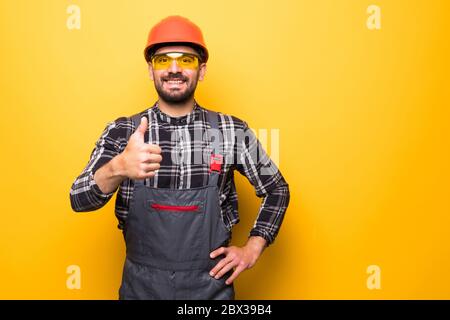 Portrait of a construction worker with hardhat making thumbs up sign on yellow background Stock Photo