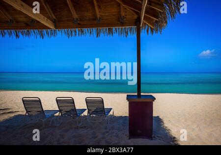 Sun Lounger chairs under a hut on an empty Seven Mile Beach in the Caribbean during confinement, Grand Cayman, Cayman Islands Stock Photo