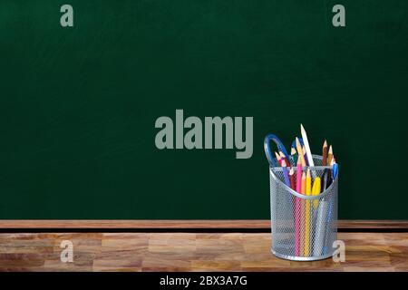 Education back-to-school concept in empty classroom setting showing pencil holder and stationaries on table with copy space on chalkboard. Stock Photo