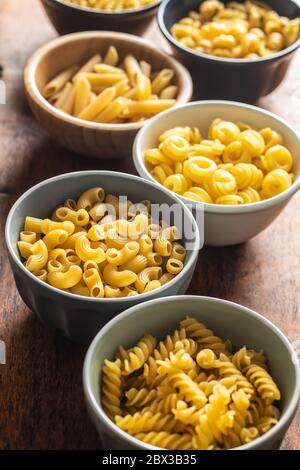 Various types of raw italian pasta in bowls on kitchen table. Stock Photo