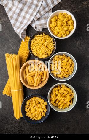 Various types of raw italian pasta in bowls on kitchen table. Top view. Stock Photo