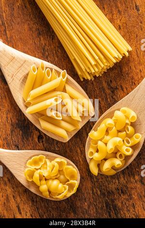 Various types of raw italian pasta in wooden spoons on wooden table. Top view. Stock Photo
