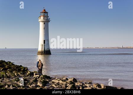 Couple on the breakwater by New Brighton lighthouse, calm waters on River Mersey, New Brighton, Wallasey Stock Photo
